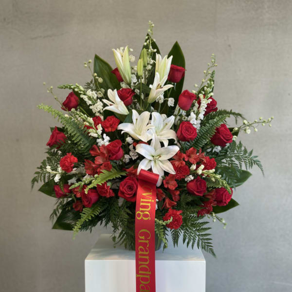 Red roses and white lilies arranged in a vase with a red ribbon