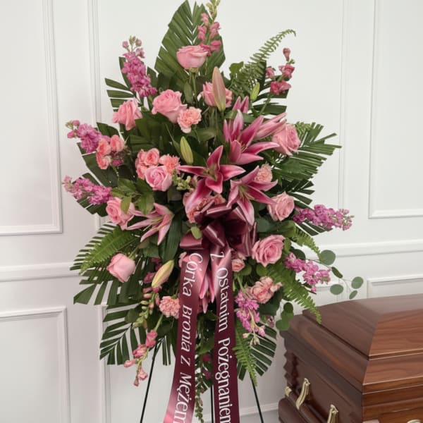 Pink roses and lilies in a standing spray with a burgundy ribbon
