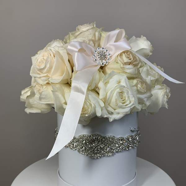 White roses arranged in a round hat box with a satin ribbon