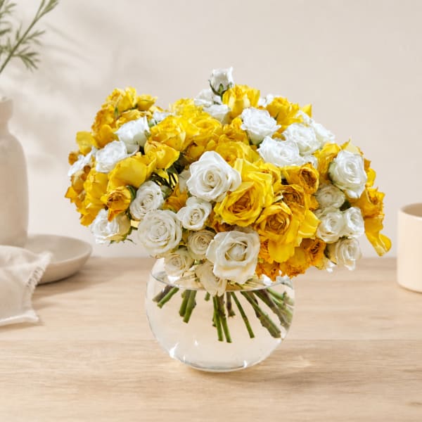 Yellow and white roses arranged in a clear glass bowl vase