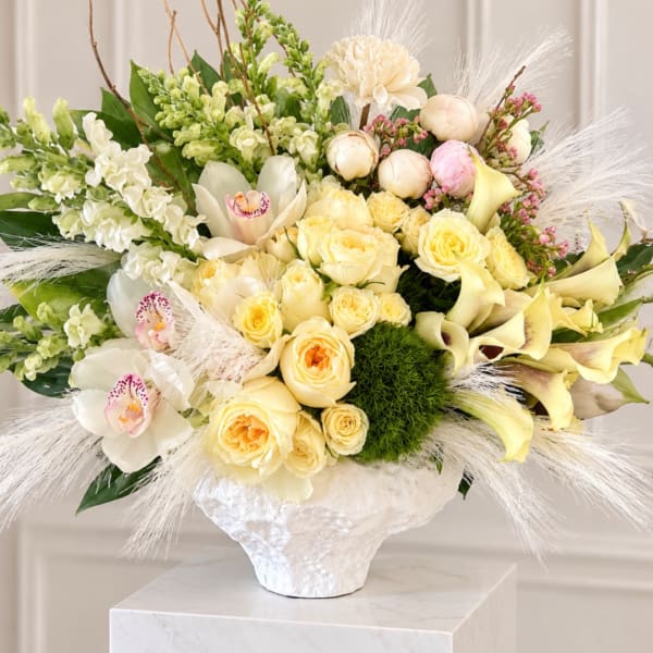 Cream floral arrangement in a white vase with roses, orchids, and calla lilies