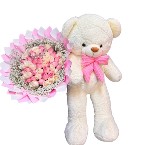 Pink and cream rose bouquet beside a white teddy bear with a pink bow