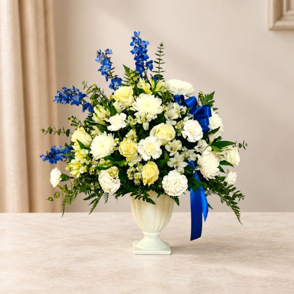 White and yellow flower arrangement in a cream vase with blue accents