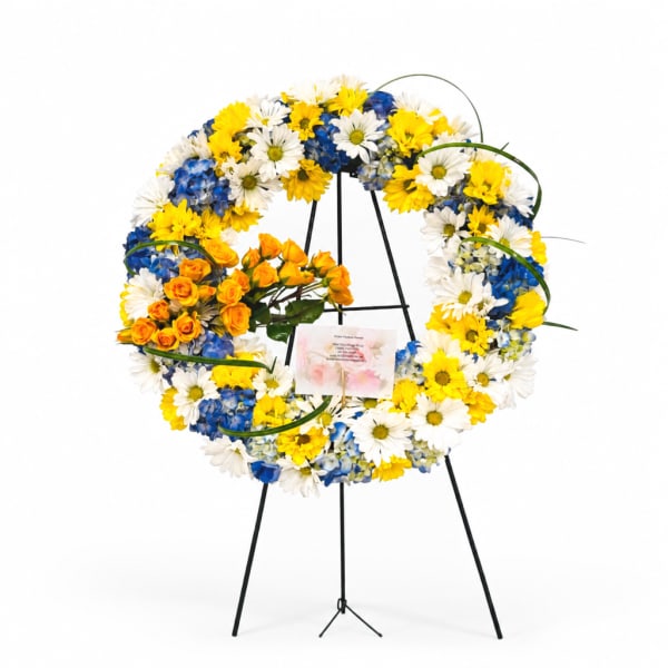 Circular standing wreath of white, yellow, and blue flowers on a black easel