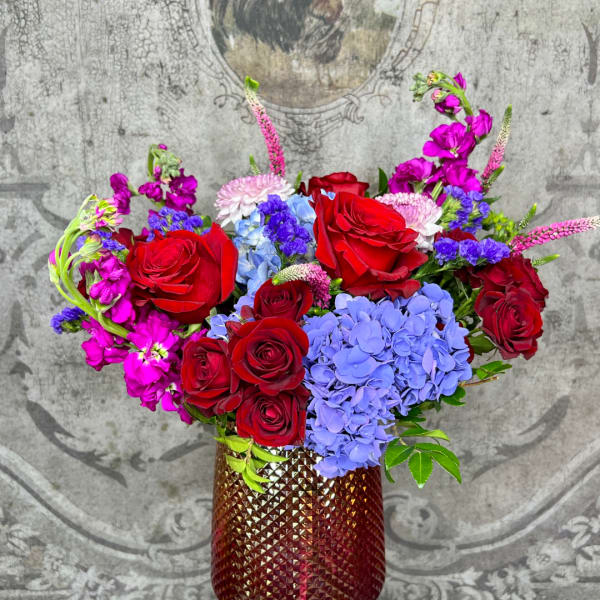 Bouquet of red roses, blue hydrangeas, and pink flowers in a textured vase