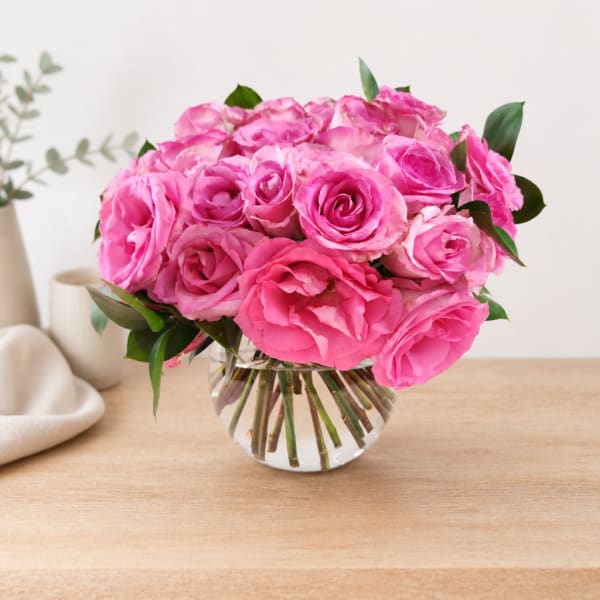Pink rose bouquet in a clear glass vase on a wooden table