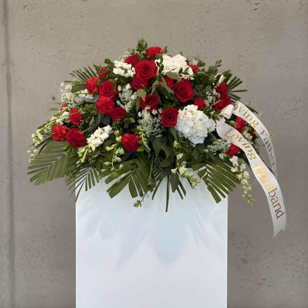 Red and white floral spray on a white stand with a ribbon