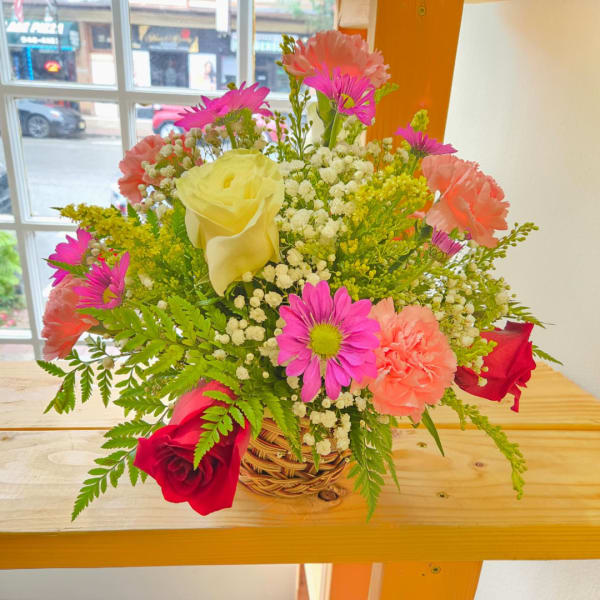 Mixed bouquet in a wicker basket with roses, carnations, and daisies
