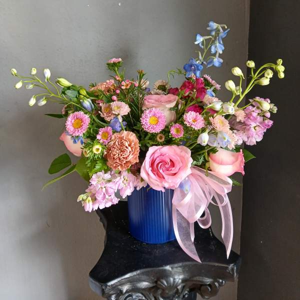 Pink and blue mixed flower arrangement in a blue vase with a pink ribbon