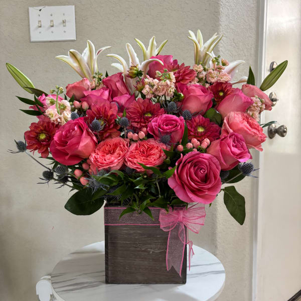 Pink roses and lilies arranged in a square box with a pink ribbon