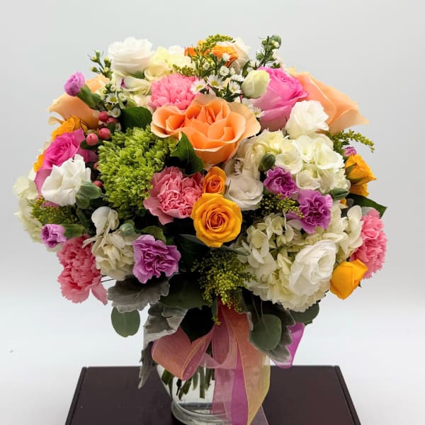 Mixed bouquet of roses, carnations, and hydrangeas in a glass vase