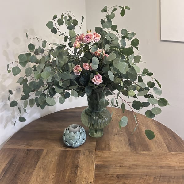Pink spray roses in a green glass vase with large eucalyptus branches
