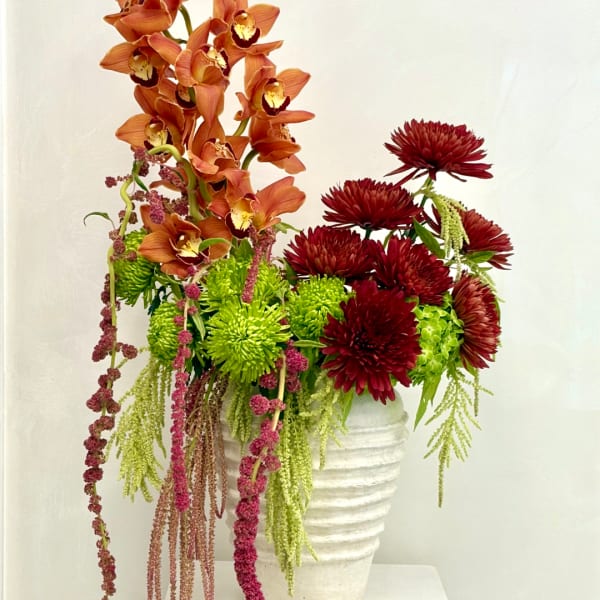 Orange orchids and burgundy mums in a white vase