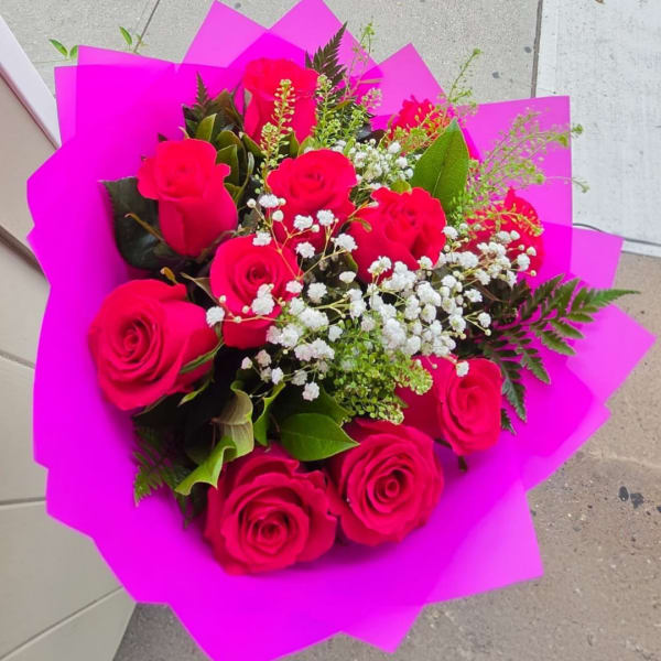 Bouquet of hot pink roses with white filler flowers wrapped in bright pink paper