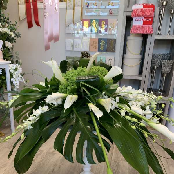 White calla lilies and orchids arranged in a white pedestal vase