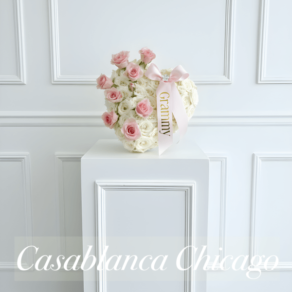 Pink and white rose arrangement with a pink ribbon on a pedestal