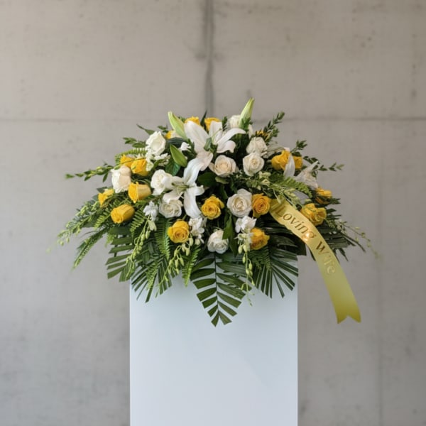 White and yellow floral arrangement on a pedestal with a ribbon
