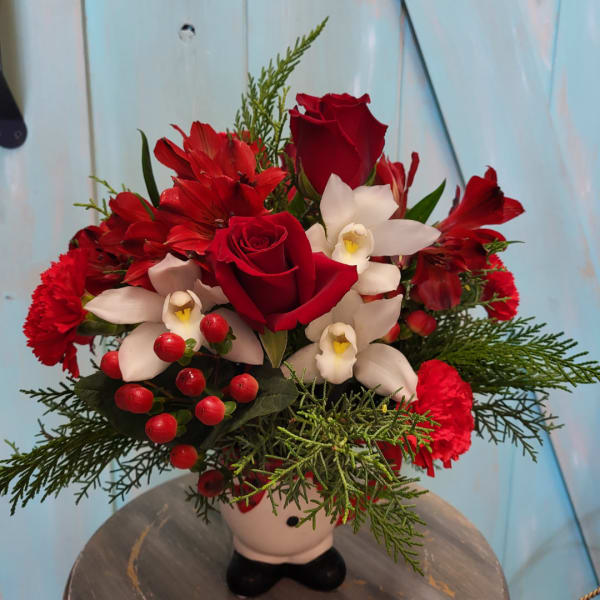 Red roses and white orchids arranged in a small vase with greenery and berries