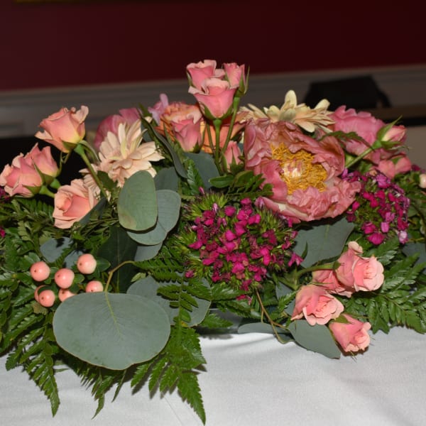 Pink roses and mixed blooms arranged low with greenery in a table centerpiece