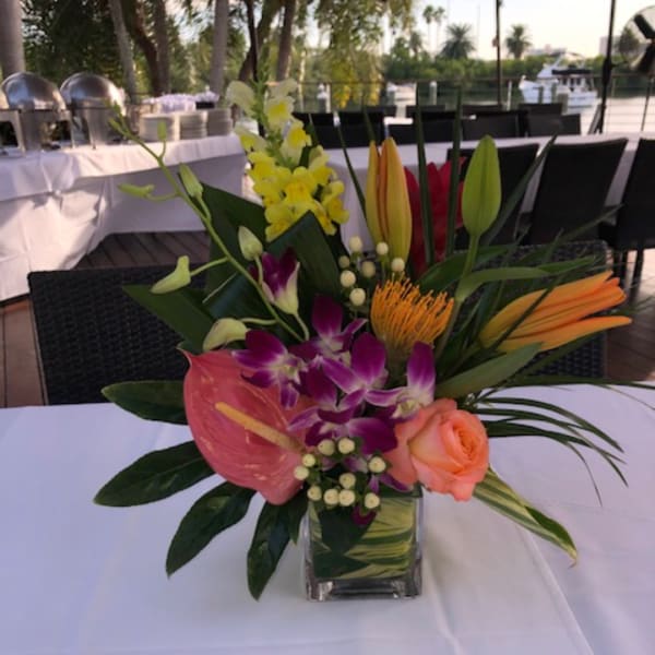 Tropical flower arrangement in a clear square vase on a table