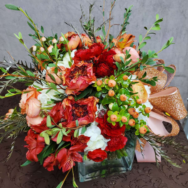 Mixed red, peach, and white bouquet in a square glass vase with glitter ribbon