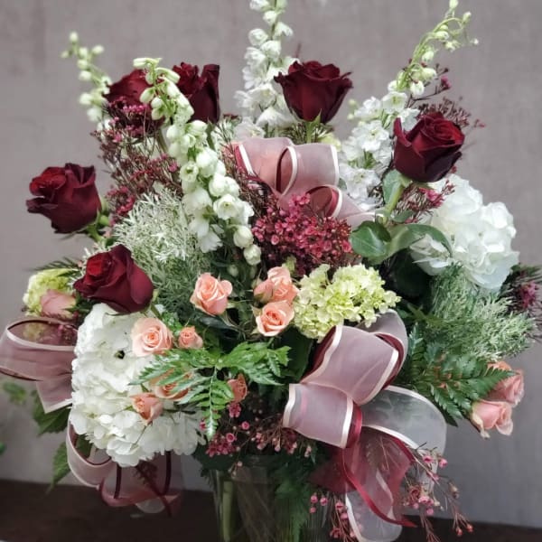 Bouquet of burgundy and blush roses with white blooms in a glass vase