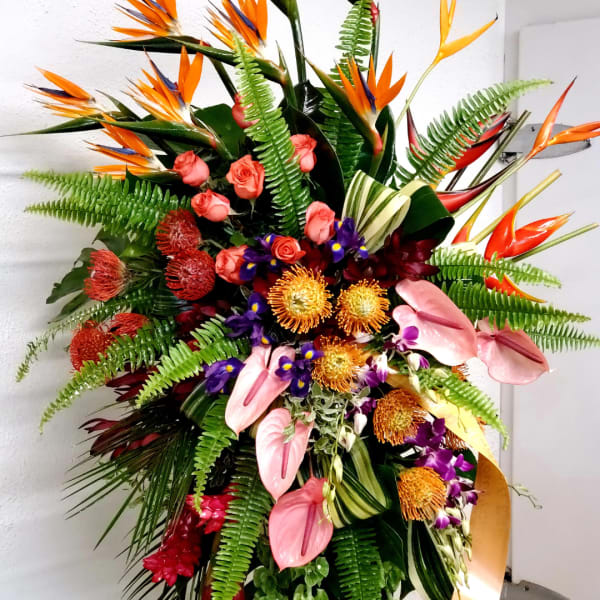 Large tropical flower arrangement with pink anthuriums, orange birds of paradise, and ferns