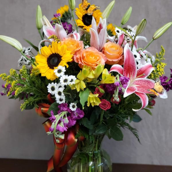 Mixed bouquet with sunflowers, pink lilies, and peach roses in a glass vase