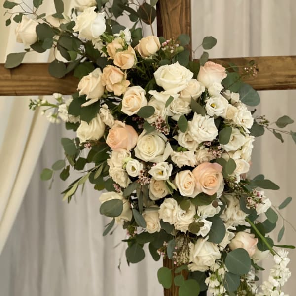 Cream and blush rose arrangement with eucalyptus on a wooden cross