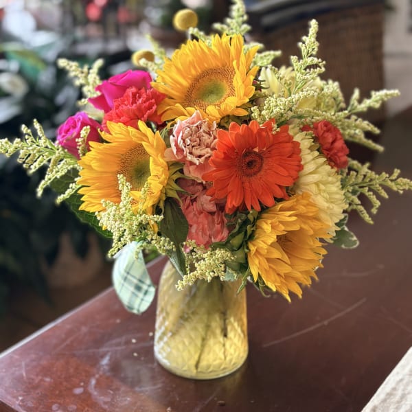 Mixed bouquet of sunflowers, roses, and gerbera daisies in a gold vase