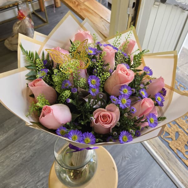 Pink roses and purple daisies in a glass vase with decorative wrap