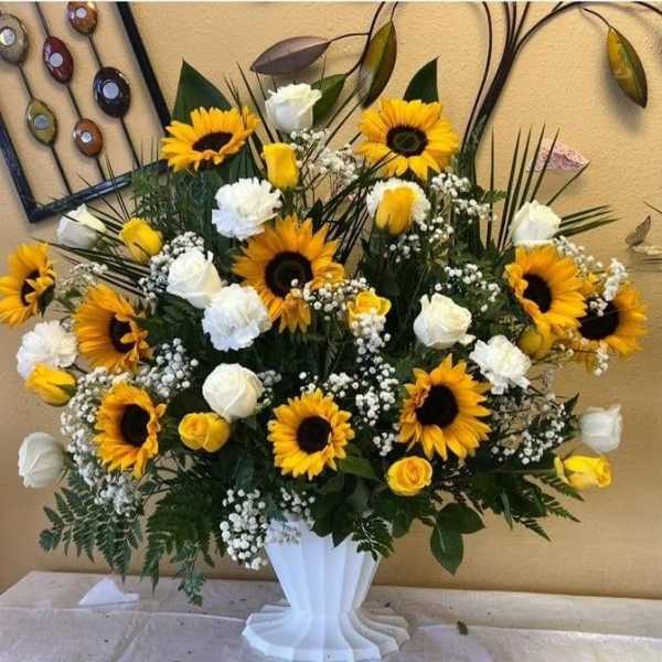 Large sunflower and white rose arrangement in a white pedestal vase