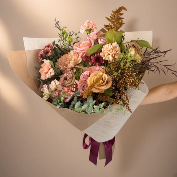 Handheld bouquet of pink and peach flowers wrapped in paper