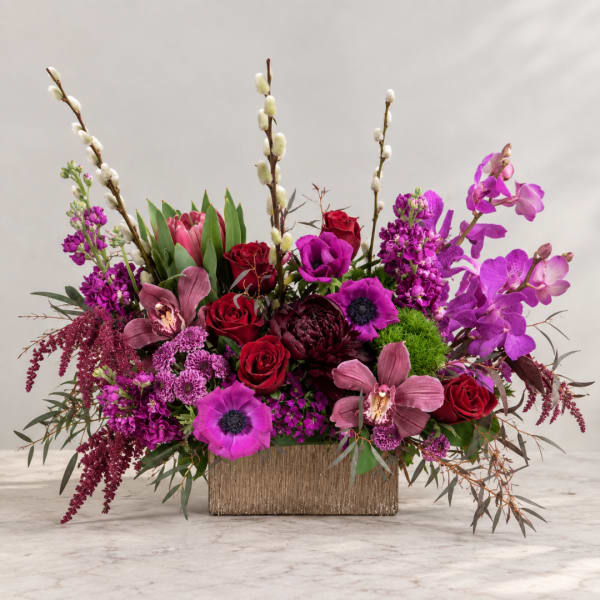Mixed bouquet of red, pink, and purple flowers in a rectangular vase