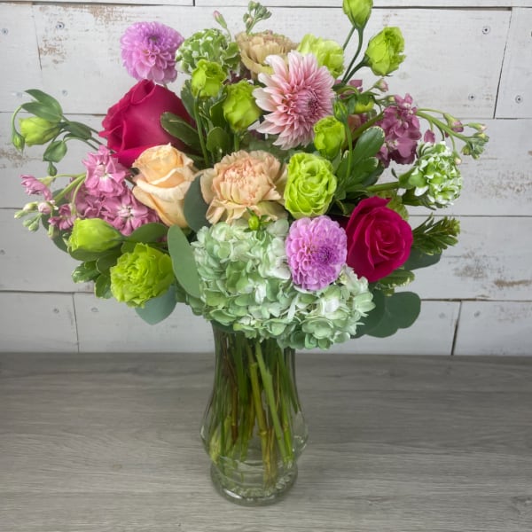 Mixed pink, green, and peach flowers in a clear glass vase