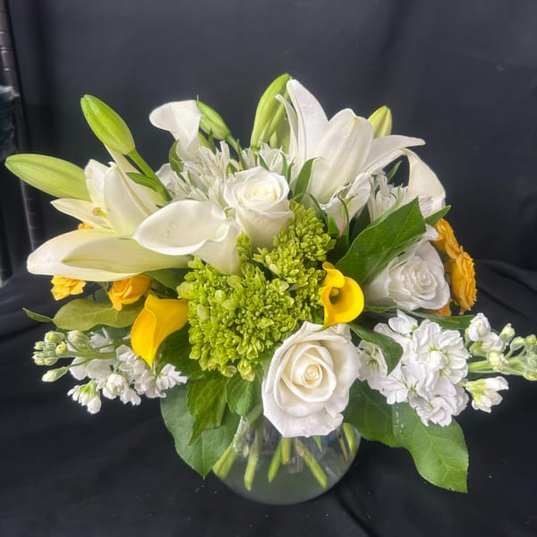 White lilies, roses, and yellow calla lilies in a glass vase