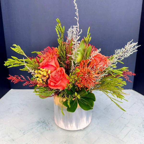 Coral roses and orange pincushion blooms in a clear vase