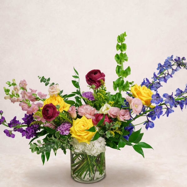 Mixed bouquet of roses, snapdragons, and blue delphinium in a glass vase