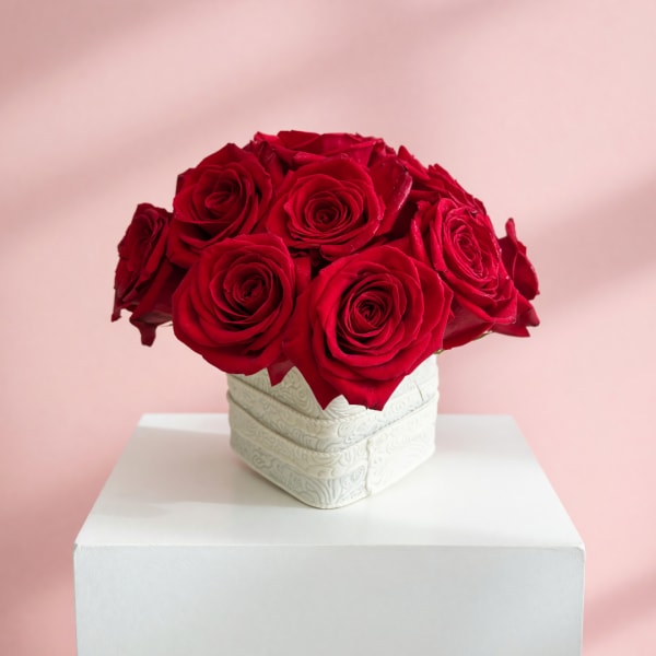 Red roses arranged in a white square vase on a pedestal