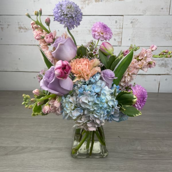 Pastel bouquet of roses, hydrangeas, and mixed blooms in a clear glass vase