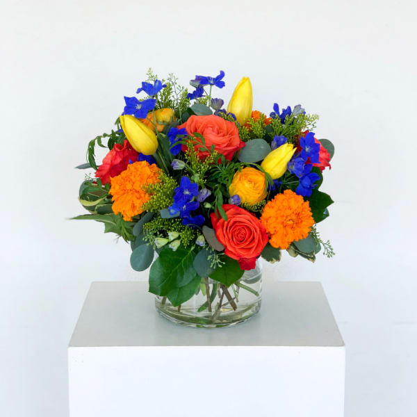 Colorful bouquet of roses, tulips, and orange blooms in a glass vase