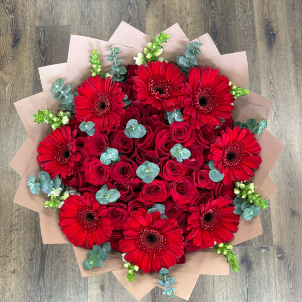 Bouquet of red roses and red gerbera daisies with pale wrapping
