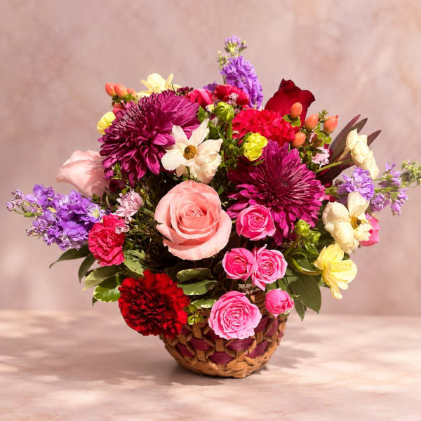 Mixed bouquet in a woven basket with pink, purple, red, and cream flowers