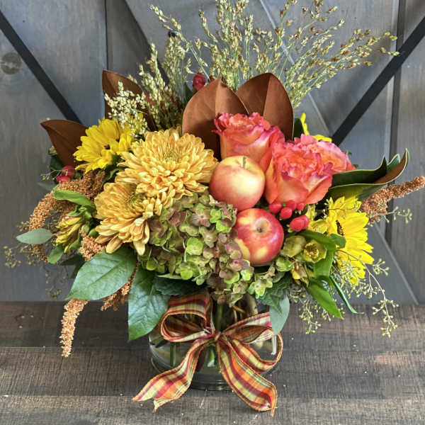 Autumn bouquet with yellow chrysanthemums, pink roses, and apples in a glass vase