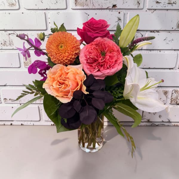 Mixed bouquet of roses, lilies, and orange blooms in a clear glass vase