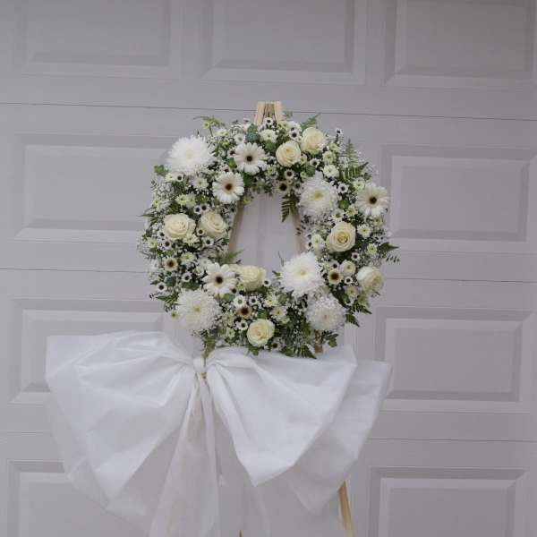 White floral wreath on a wooden easel with a large white bow