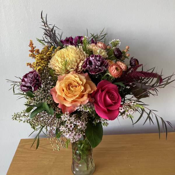 Mixed bouquet of roses, chrysanthemums, and small filler flowers in a glass vase