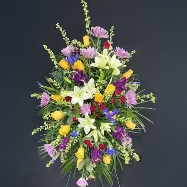 Tall standing spray with yellow roses, white lilies, and mixed purple flowers on an easel