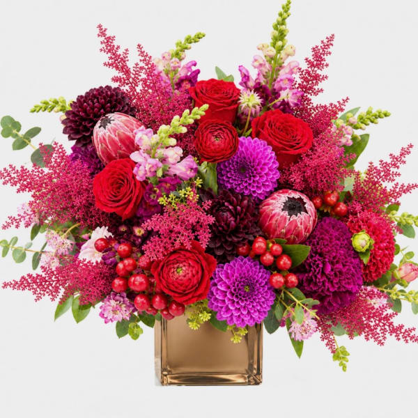Bright mixed bouquet in a square glass vase with red, pink, and purple blooms