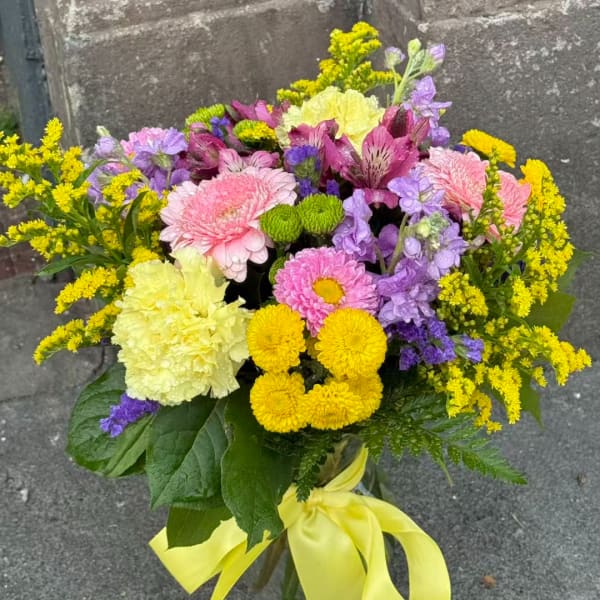 Mixed bouquet of pink, yellow, and purple flowers in a glass vase with a yellow ribbon